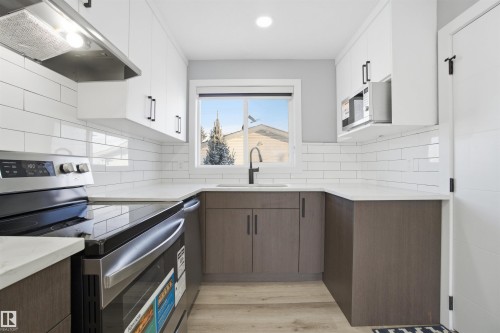 Modern kitchen featuring white upper cabinets and dark lower cabinets, white countertops, subway tile backsplash, and stainless steel appliances - 5208 90 Avenue, Edmonton, AB - Indoor Photo Showing Kitchen