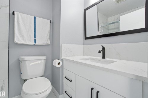 Bathroom featuring a white vanity with black hardware, a rectangular sink with a black faucet, and a large mirror with a black frame - 5208 90 Avenue, Edmonton, AB - Indoor Photo Showing Bathroom