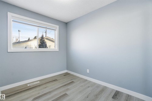 This room features light blue walls, a large window with white trim, and light-colored plank flooring - 5208 90 Avenue, Edmonton, AB - Indoor Photo Showing Other Room
