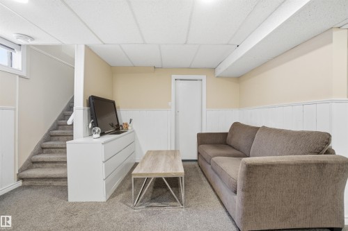 This room features neutral-toned carpet, light beige walls with white wainscoting, and a drop panel ceiling - 5208 90 Avenue, Edmonton, AB - Indoor