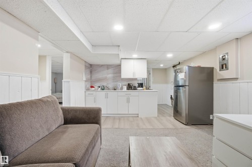 The property features a bright living area with recessed lighting, wainscoting, and a compact kitchen area equipped with white cabinetry and a stainless steel refrigerator - 5208 90 Avenue, Edmonton, AB - Indoor
