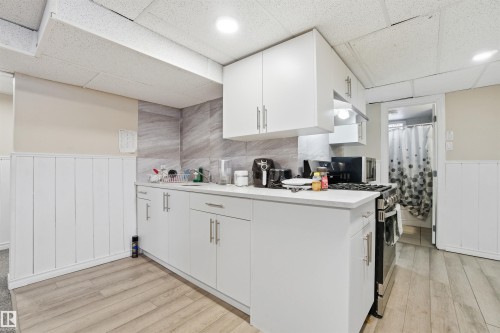 This kitchen features white cabinetry with brushed nickel hardware, a light-colored countertop, and a tiled backsplash - 5208 90 Avenue, Edmonton, AB - Indoor