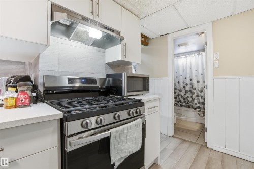 The kitchen features a stainless steel range with a matching range hood, white cabinetry, and light-colored countertops - 5208 90 Avenue, Edmonton, AB - Indoor Photo Showing Kitchen