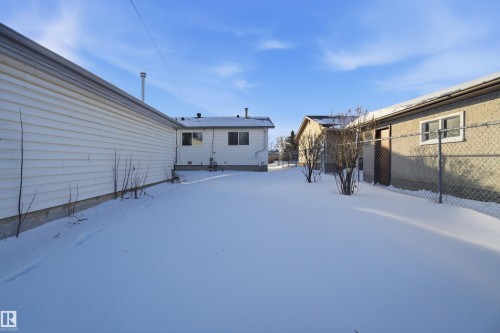 The property includes a spacious outdoor area blanketed in snow, featuring a chain-link fence and mature shrubs - 5208 90 Avenue, Edmonton, AB - Outdoor With Exterior