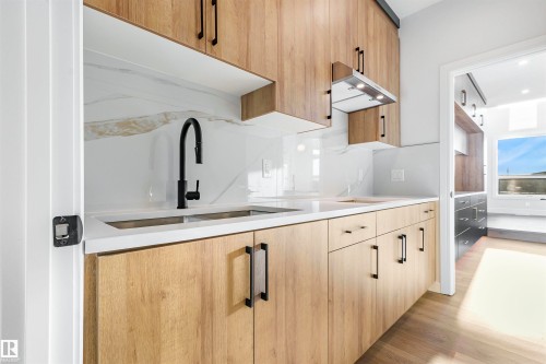 Modern kitchen featuring wood-finish cabinetry with matte black hardware, white countertops, and a white marble-patterned backsplash - 372 Creekside Green, Leduc, AB - Indoor Photo Showing Kitchen