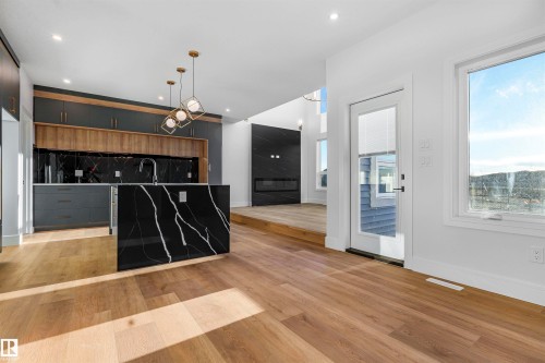 Modern kitchen featuring a waterfall island with a black and white patterned surface, a black backsplash, and a combination of wood-finish and dark cabinetry - 372 Creekside Green, Leduc, AB - Indoor