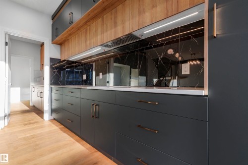 Contemporary kitchen featuring dark gray cabinetry, wood-finish accent shelving, and a dark stone-patterned backsplash - 372 Creekside Green, Leduc, AB - Indoor