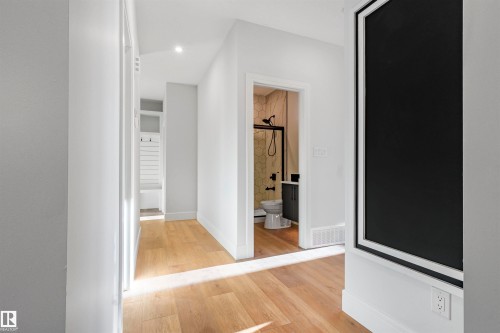 Hallway with wood-finish flooring and recessed lighting, leading to a bathroom featuring a walk-in shower with a black-framed glass enclosure, hexagonal tile walls, and a dark vanity - 372 Creekside Green, Leduc, AB - Indoor Photo Showing Other Room