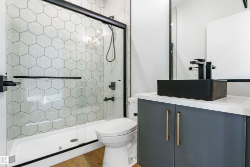 Modern bathroom featuring a glass-enclosed shower with geometric hexagonal tiling, matte black fixtures, a contemporary vessel sink, and a vanity with gold-tone hardware - 372 Creekside Green, Leduc, AB - Indoor Photo Showing Bathroom