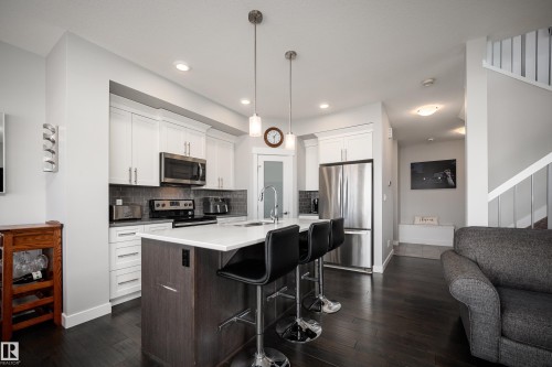 Modern kitchen featuring white cabinetry, stainless steel appliances, a dark tile backsplash, a central island with bar seating, and dark wood-finish flooring - 2704 Koshal Place, Edmonton, AB - Indoor Photo Showing Kitchen With Upgraded Kitchen