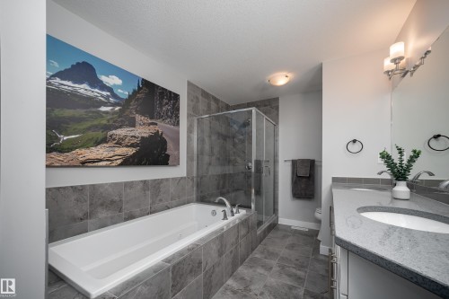 Bathroom featuring a built-in white soaking tub, a glass-enclosed shower, a dual-sink vanity with light-toned countertops, and gray tile flooring - 2704 Koshal Place, Edmonton, AB - Indoor Photo Showing Bathroom
