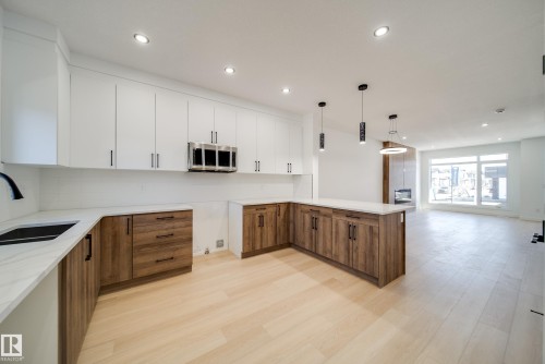 Open-concept kitchen featuring two-tone cabinetry, a central island, recessed lighting, and wood-finish flooring - 86 Blackbird Bend, Fort Saskatchewan, AB - Indoor Photo Showing Kitchen