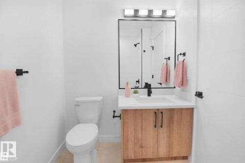 Bathroom featuring a white toilet, light wood-finish vanity with a white countertop, rectangular sink, and matte black hardware - 86 Blackbird Bend, Fort Saskatchewan, AB - Indoor Photo Showing Bathroom