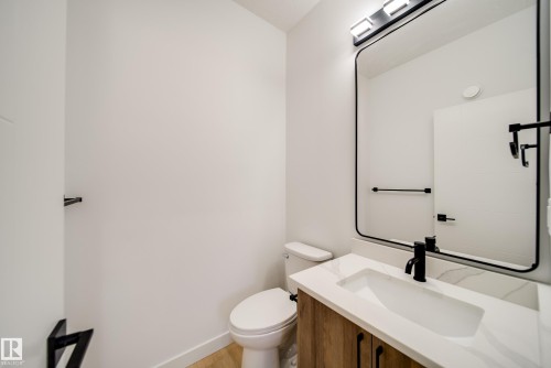 Bathroom vanity featuring a white rectangular sink, a white countertop with subtle veining, and a wood-finish cabinet with matte black hardware - 86 Blackbird Bend, Fort Saskatchewan, AB - Indoor Photo Showing Bathroom
