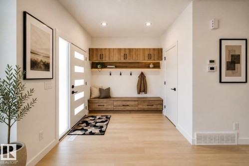 Entryway featuring light wood-finish flooring, a contemporary white entry door with frosted glass panels, and a built-in wood-finish storage bench with drawers - 86 Blackbird Bend, Fort Saskatchewan, AB - Indoor Photo Showing Other Room