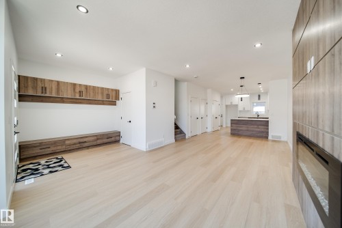 Bright open-concept living space featuring light wood-finish flooring, recessed ceiling lighting, and a modern fireplace with a textured surround - 86 Blackbird Bend, Fort Saskatchewan, AB - Indoor Photo Showing Other Room