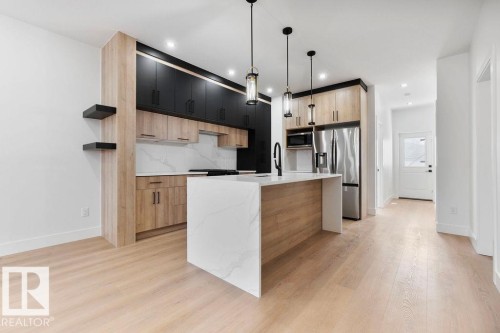 Modern kitchen featuring light-colored flooring, two-toned cabinetry, a spacious island with a white countertop, and stainless steel appliances - 12307 91 St Nw, Edmonton, AB - Indoor Photo Showing Kitchen With Upgraded Kitchen