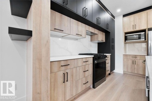 The kitchen features light wood cabinetry with dark hardware, white countertops, and a full-height white backsplash - 12307 91 St Nw, Edmonton, AB - Indoor Photo Showing Kitchen With Upgraded Kitchen