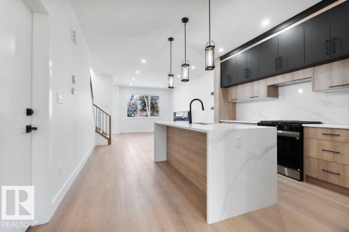 The kitchen features a large island with a waterfall countertop, a matte black faucet, and pendant lighting - 12307 91 St Nw, Edmonton, AB - Indoor Photo Showing Kitchen With Upgraded Kitchen