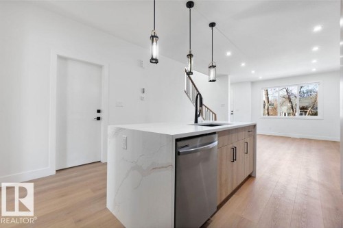The kitchen features a waterfall island with a stainless steel dishwasher, a black faucet, and pendant lighting - 12307 91 St Nw, Edmonton, AB - Indoor Photo Showing Kitchen