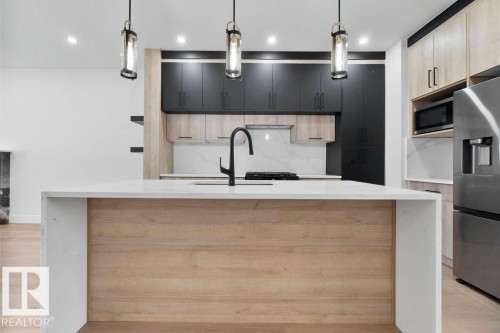 Modern kitchen featuring a large island with a light wood panel accent and a white countertop, dark and light wood cabinetry, and a stainless steel refrigerator - 12307 91 St Nw, Edmonton, AB - Indoor Photo Showing Kitchen With Upgraded Kitchen