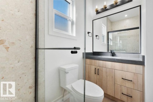 This bathroom features a contemporary vanity with a dark countertop and light wood cabinetry, a large mirror with integrated lighting, and a white toilet - 12307 91 St Nw, Edmonton, AB - Indoor Photo Showing Bathroom