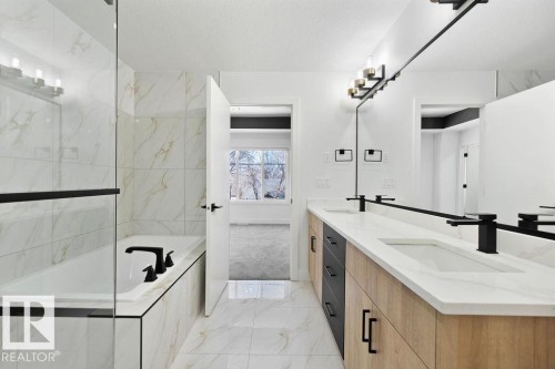 A contemporary bathroom featuring a bathtub with a tiled surround, a glass shower enclosure, and a double vanity with white countertops and matte black fixtures - 12307 91 St Nw, Edmonton, AB - Indoor Photo Showing Bathroom