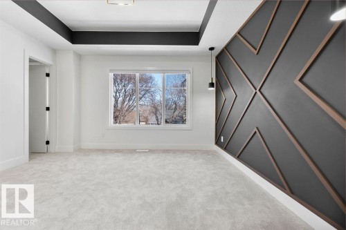Spacious room featuring light-colored carpeting, a large window, and a decorative accent wall with geometric wood paneling - 12307 91 St Nw, Edmonton, AB - Indoor Photo Showing Other Room