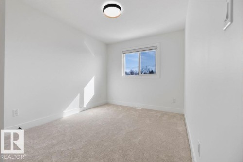 This bright room features a large window, light-colored carpeting, white walls, and a modern ceiling light fixture - 12307 91 St Nw, Edmonton, AB - Indoor Photo Showing Other Room