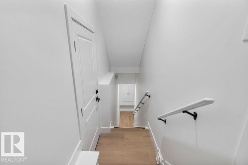 The property features a bright hallway with white walls and light wood flooring, leading to a white door with black hardware - 12307 91 St Nw, Edmonton, AB - Indoor Photo Showing Other Room