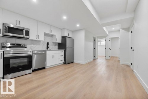 The property features a modern kitchen equipped with stainless steel appliances, white cabinetry, and a marble-patterned backsplash - 12307 91 St Nw, Edmonton, AB - Indoor Photo Showing Kitchen With Stainless Steel Kitchen