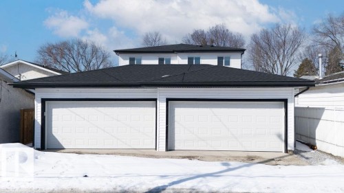 The property features two white garage doors with black trim, a black shingled roof, and white siding - 12307 91 St Nw, Edmonton, AB - Outdoor With Exterior