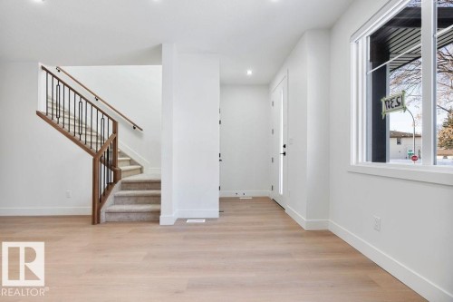 Entryway featuring light hardwood flooring, a staircase with carpeted treads and a dark wood and black metal railing, and a window with white trim - 12307 91 St Nw, Edmonton, AB - Indoor Photo Showing Other Room