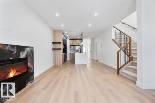 Living area featuring light wood flooring, a fireplace with a dark marble-look surround, recessed lighting, and a staircase with wood and black metal railings - 12307 91 St Nw, Edmonton, AB - Indoor With Fireplace