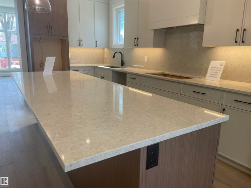 Expansive kitchen island with a light-toned countertop, wood-finish base, and integrated electrical outlets - 14344 92A Avenue, Edmonton, AB - Indoor Photo Showing Kitchen With Upgraded Kitchen