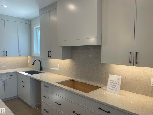 Contemporary kitchen featuring light gray cabinetry with black hardware, a black single-basin sink with a matte black faucet, and light-toned countertops extending as a full backsplash - 14344 92A Avenue, Edmonton, AB - Indoor Photo Showing Kitchen
