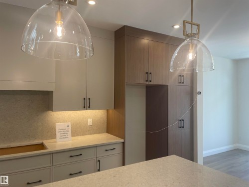 Kitchen featuring pendant lighting, light-toned cabinetry, wood-finish paneling, under-cabinet lighting, and stone countertops - 14344 92A Avenue, Edmonton, AB - Indoor Photo Showing Kitchen