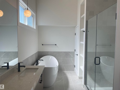 Modern bathroom featuring a freestanding tub, glass-enclosed shower, a double vanity with integrated sinks, and matte black fixtures - 14344 92A Avenue, Edmonton, AB - Indoor Photo Showing Bathroom