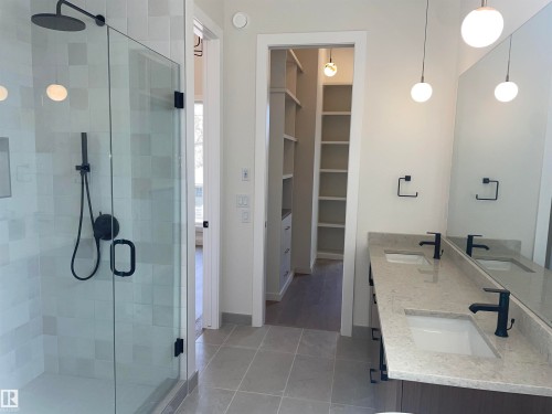 Bathroom featuring a glass-enclosed shower with matte black fixtures, dual vanity with undermount sinks, stone countertops, and spherical pendant lighting - 14344 92A Avenue, Edmonton, AB - Indoor Photo Showing Bathroom