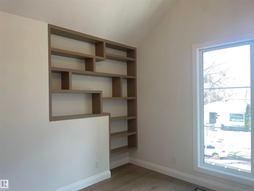 Built-in shelving unit with varied cubby sizes, natural light from a large window, light-toned wood-finish flooring, white baseboards, and a vaulted ceiling - 14344 92A Avenue, Edmonton, AB - Indoor