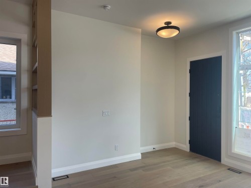 Spacious room featuring light wood-finish flooring, white baseboards, and a dark paneled door - 14344 92A Avenue, Edmonton, AB - Indoor Photo Showing Other Room