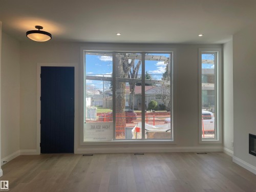 Bright interior space featuring oversized windows, wood-finish flooring, recessed lighting, a modern flush-mount light fixture, and a built-in fireplace - 14344 92A Avenue, Edmonton, AB - Indoor With Fireplace
