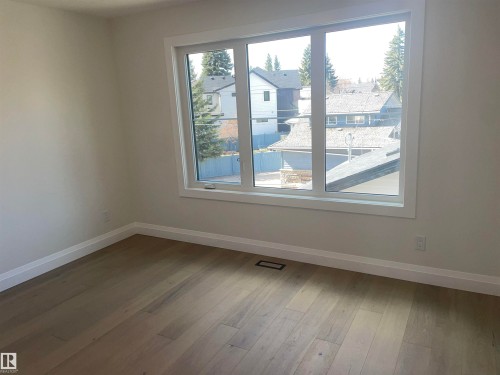 Vaulted ceiling featuring a geometric black light fixture, two tall windows with white trim, light wood-finish flooring, and crisp white baseboards - 14344 92A Avenue, Edmonton, AB - Indoor Photo Showing Other Room