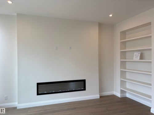 Linear electric fireplace with a black frame, recessed built-in shelving, wood-finish flooring, white baseboards, and neutral wall paint - 14344 92A Avenue, Edmonton, AB - Indoor With Fireplace