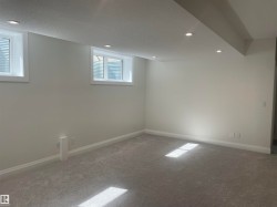Spacious room featuring light gray carpeting, recessed ceiling lighting, two egress windows, and painted baseboards - 