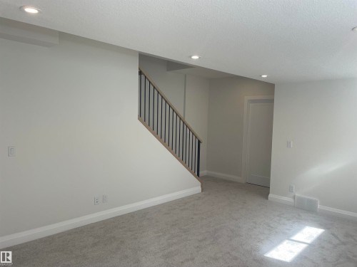 Carpeted room featuring a contemporary staircase with wood-finish handrail and black metal balusters - 14344 92A Avenue, Edmonton, AB - Indoor Photo Showing Other Room
