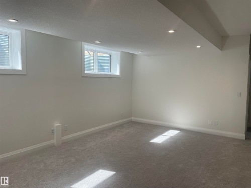 Spacious room featuring light gray carpeting, recessed ceiling lighting, two egress windows, and painted baseboards - 14344 92A Avenue, Edmonton, AB - Indoor Photo Showing Other Room