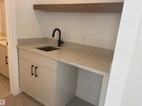 Integrated wet bar featuring a matte black faucet, dark basin sink, and light-toned stone countertop with matching backsplash - 14344 92A Avenue, Edmonton, AB - Indoor