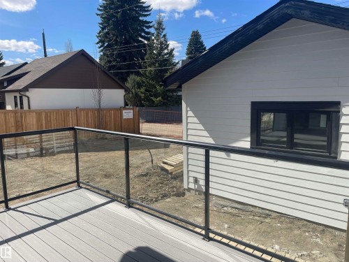 Rear exterior featuring white horizontal siding, black trim window, black soffit, and a gray composite deck with glass panel railing - 14344 92A Avenue, Edmonton, AB - Outdoor With Exterior