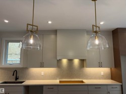 Kitchen featuring two glass dome pendant lights with brass accents, recessed ceiling lighting, light-toned cabinetry, and a textured backsplash - 